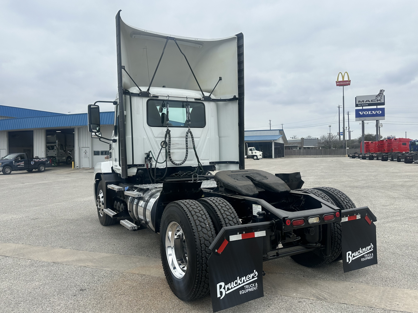 Truck chassis rear view showing fifth wheel, dual fuel tanks, rear mud flaps, and wheel axles of a 2022 Mack AN42T conventional daycab used truck.