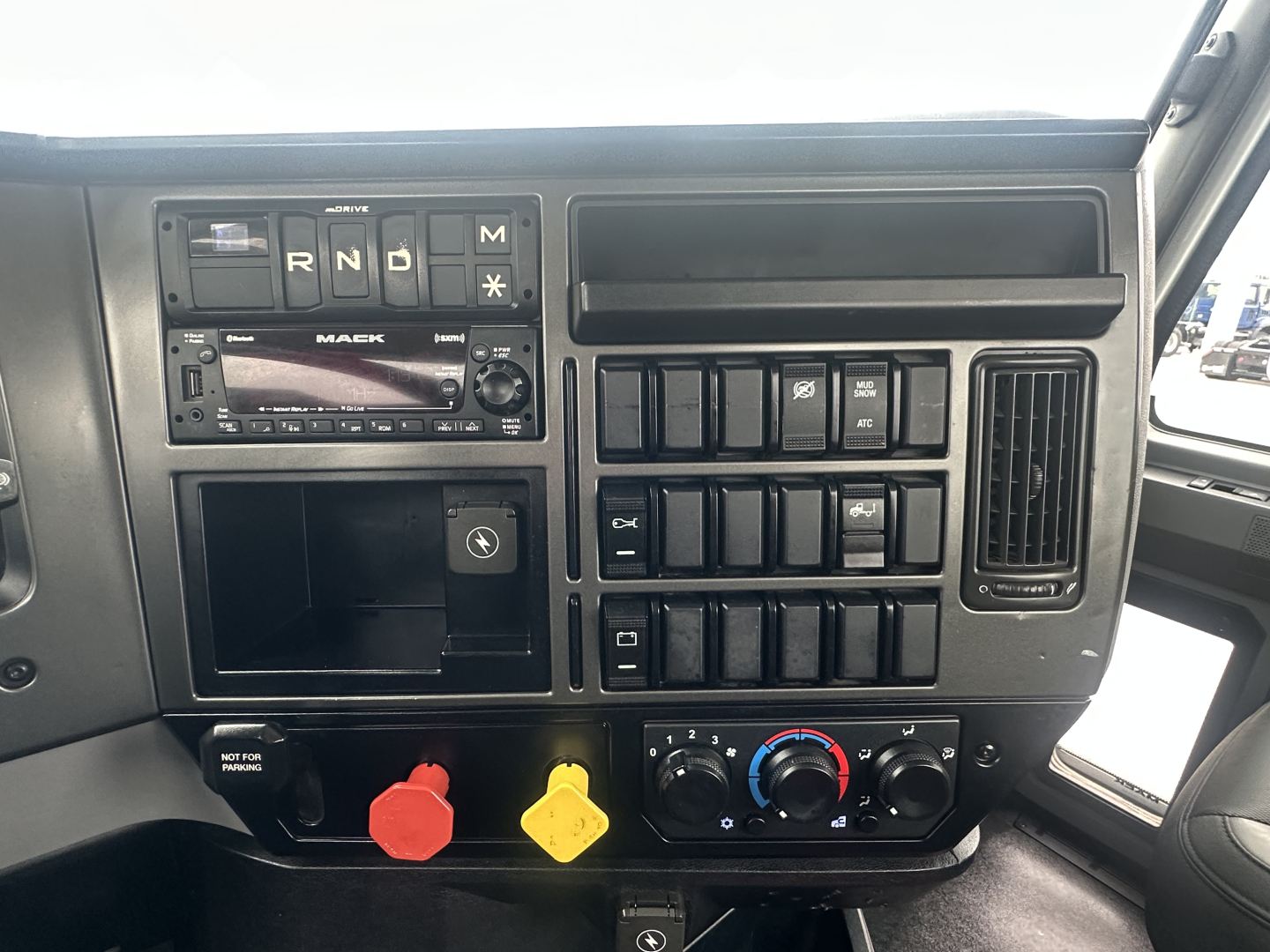 Mack AN42T interior dashboard showing gear selector, climate controls, and switches with red and yellow auxiliary caps.