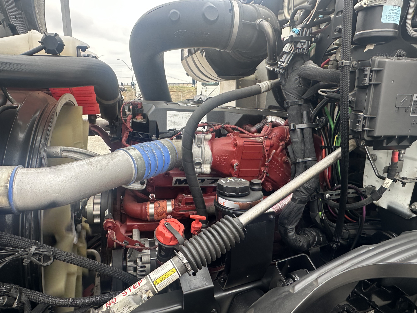 Mack AN42T engine bay showing red engine block, coolant hoses, intake pipe, and hydraulic lines.
