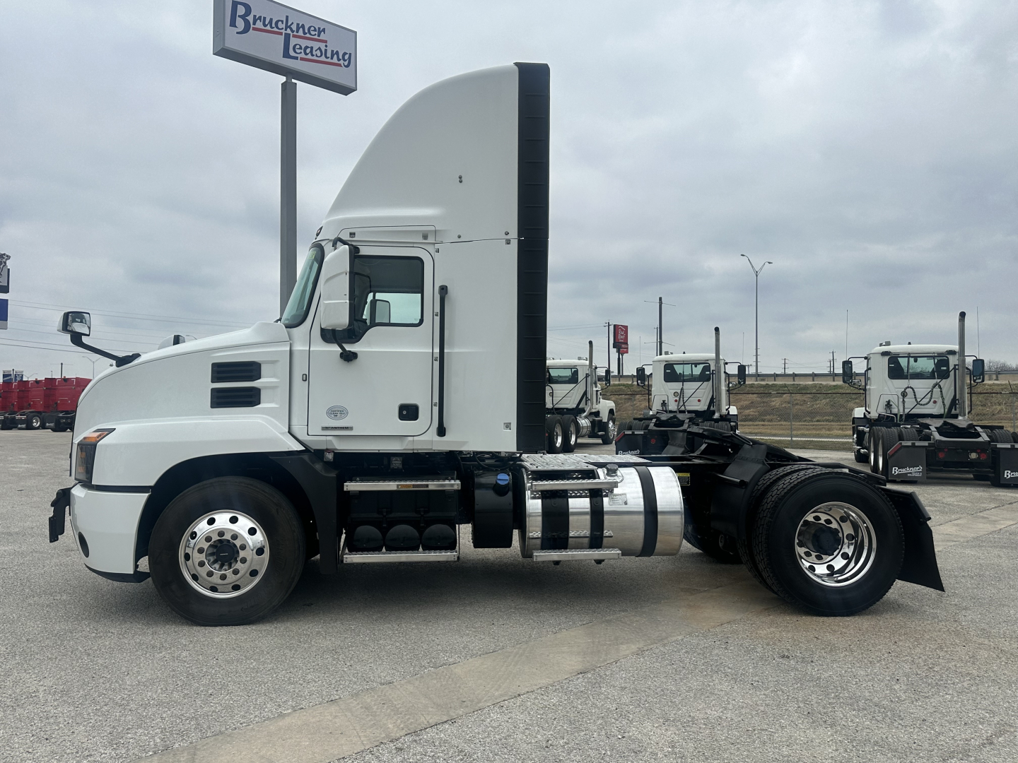 View of a 2022 Mack AN42T daycab truck chassis in a used truck lot. Side profile shows fuel tanks, exhaust stack, cab, and front tires.