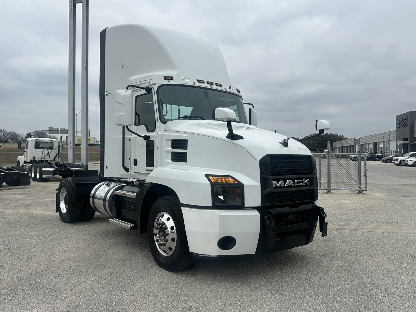 Truck cab showing 2022 Mack AN42T with white exterior, front grille with Mack emblem, dual rear axles, day cab, fuel tanks, and bumper in a dealership lot.