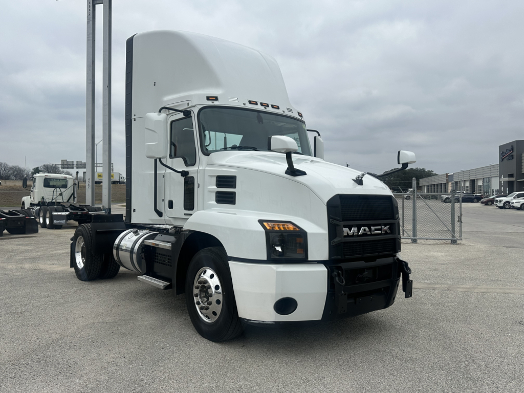 Truck cab showing 2022 Mack AN42T with white exterior, front grille with Mack emblem, dual rear axles, day cab, fuel tanks, and bumper in a dealership lot.