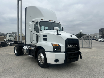Truck cab showing 2022 Mack AN42T with white exterior, front grille with Mack emblem, dual rear axles, day cab, fuel tanks, and bumper in a dealership lot.