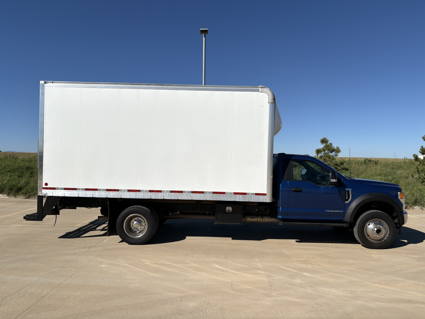 Box truck side view showing cargo box and blue cab under clear sky.