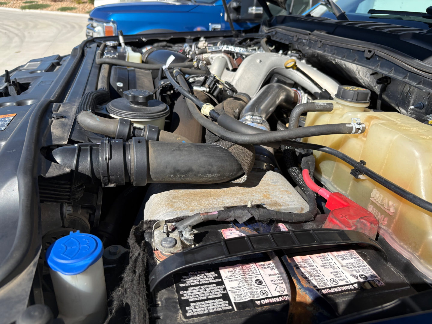 Ford F-Series engine bay showing coolant reservoir, battery, radiator support, and various hoses in a truck engine bay.