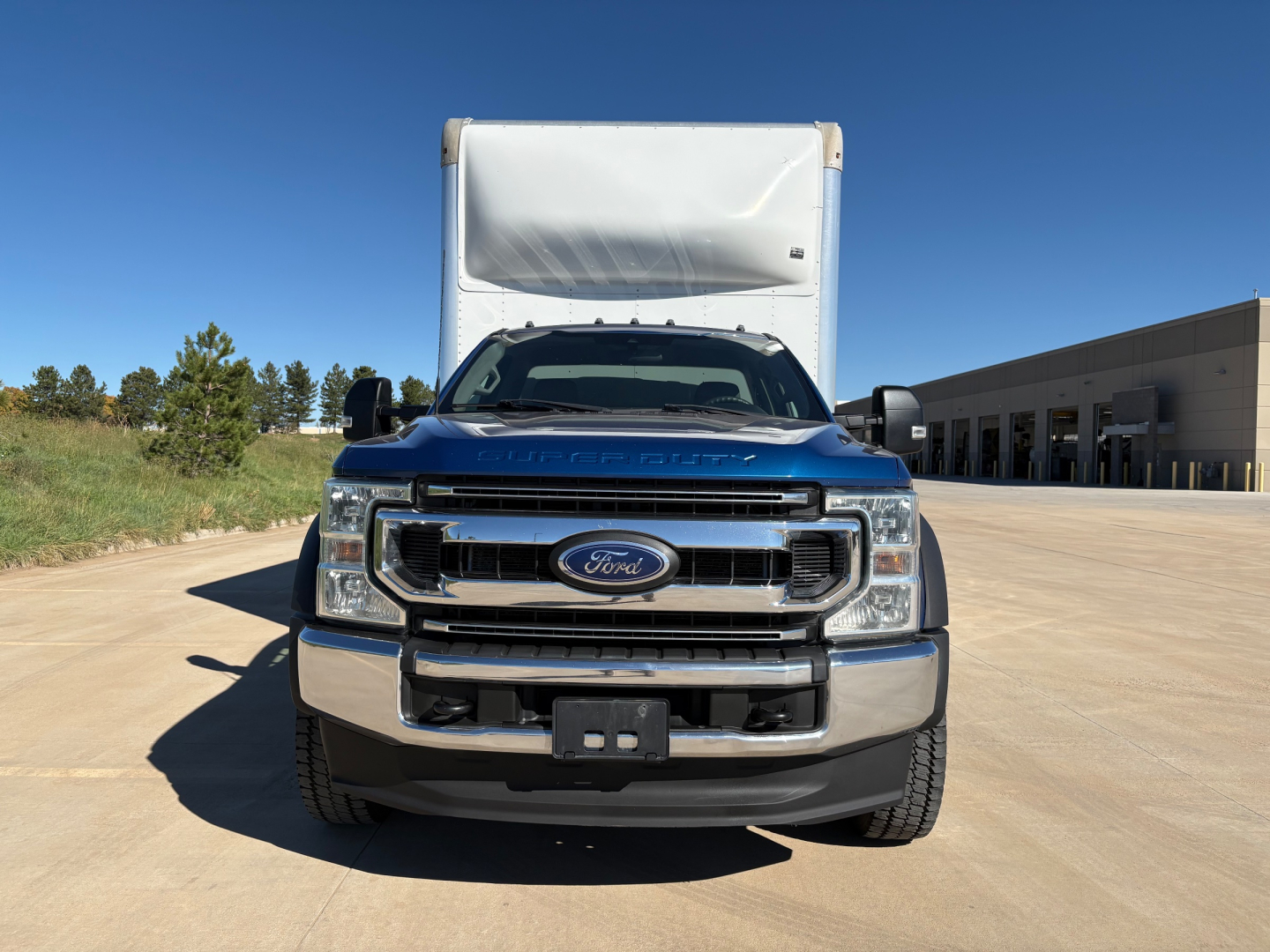 Front view of a blue 2022 Ford F-550 box truck, large chrome grille with Ford emblem, black bumper, dual headlights, white box cargo area in background.