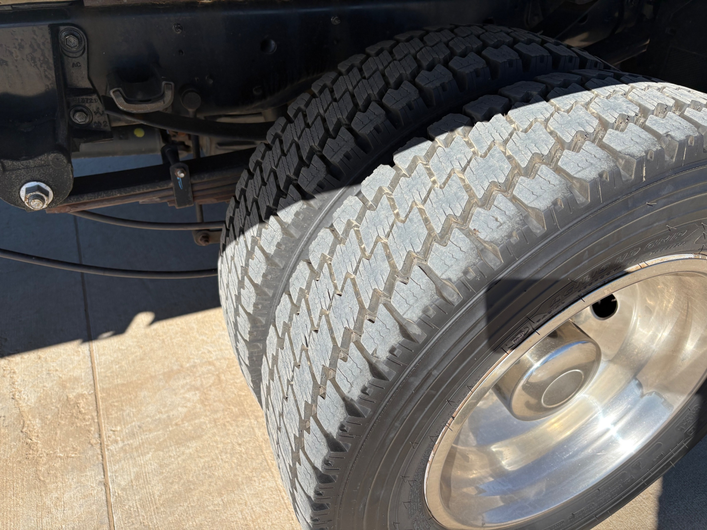Ford F550 wheel and front suspension view with dual rear dual tires and chrome hubcap, tire treads visible