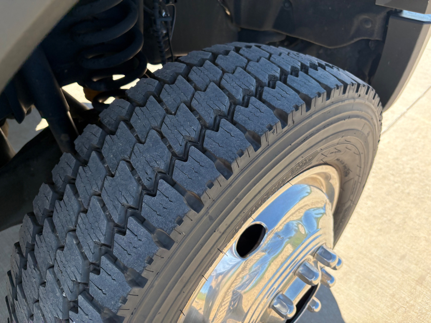 Truck wheel and tire close-up showing off-road tread over a Ford F-550. Visible text includes no explicit labeling; image focuses on tire treads and chrome wheel.