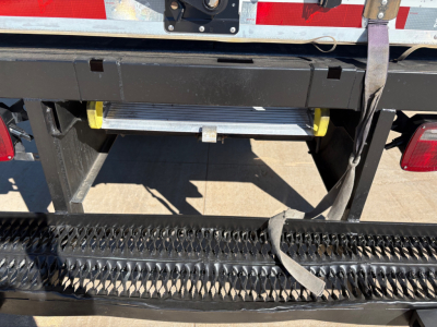Back of a 2022 Ford F550 box truck showing a fold-out step/rungs and bumper with reflective tape and a black protective mesh. Visible text includes no legible labels in the image.