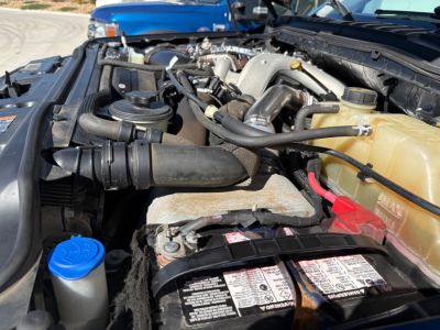 Ford F-Series engine bay showing coolant reservoir, battery, radiator support, and various hoses in a truck engine bay.