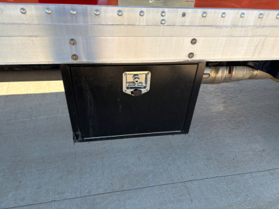 Ford F-550 underbody toolbox box with latch mounted on the side of a aluminum cargo box, visible fuel line/hoses and concrete ground.