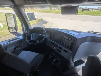 Cab interior of a Freightliner Cascadia 126 day cab showing steering wheel, dash, and driver's seat.