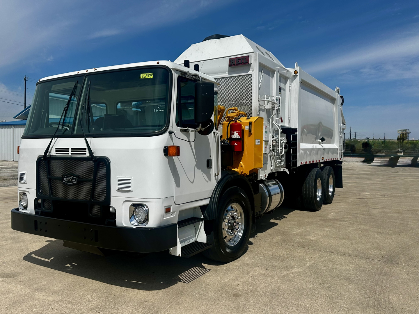 White 2019 Autocar XPEDITOR dump truck with side-mounted hydraulic arms and large hopper, front grille and headlights visible. Vehicle ID decals on windshield; no text clearly legible other than small sticker.