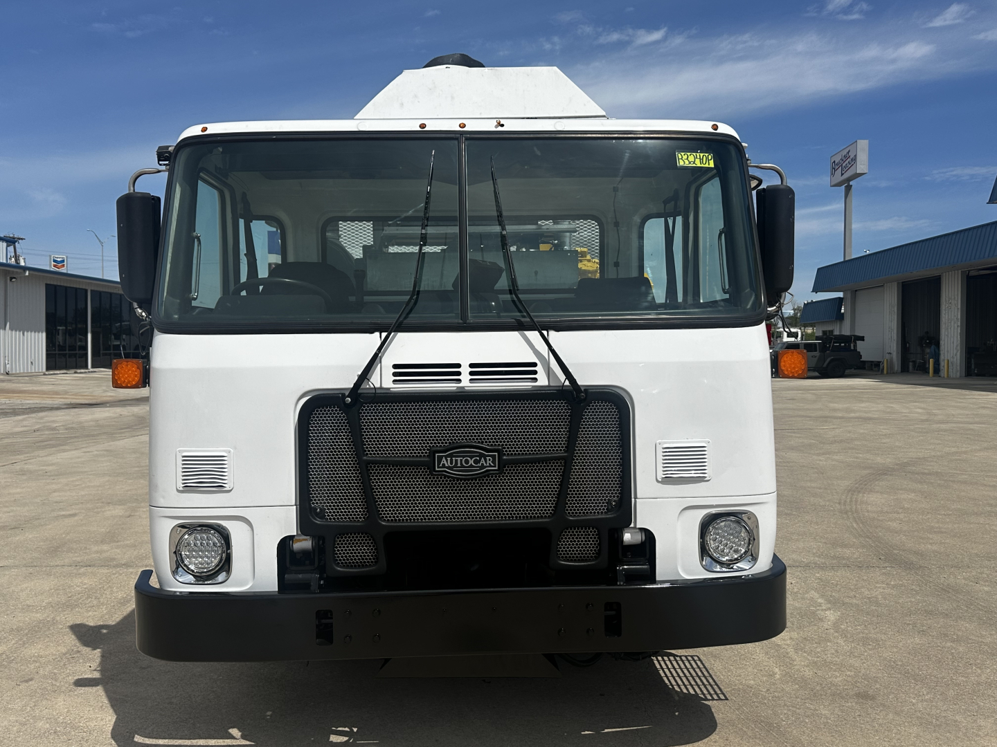 Autocar XPEDITOR truck front view showing grille, headlights, bumper, and windshield with wipers; white cab; factory badge on grille.