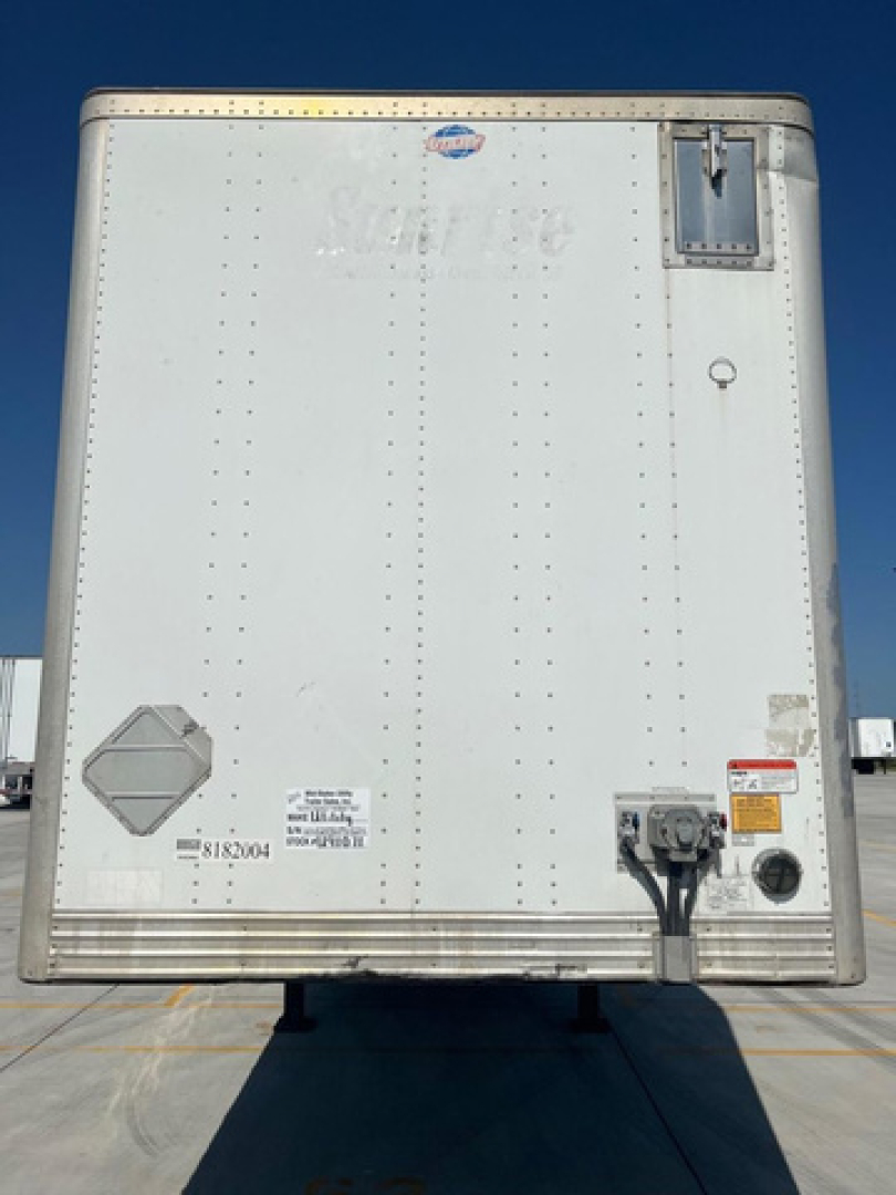 Rear view of a white utility van trailer showing VIN sticker, electrical connections, and small access doors.