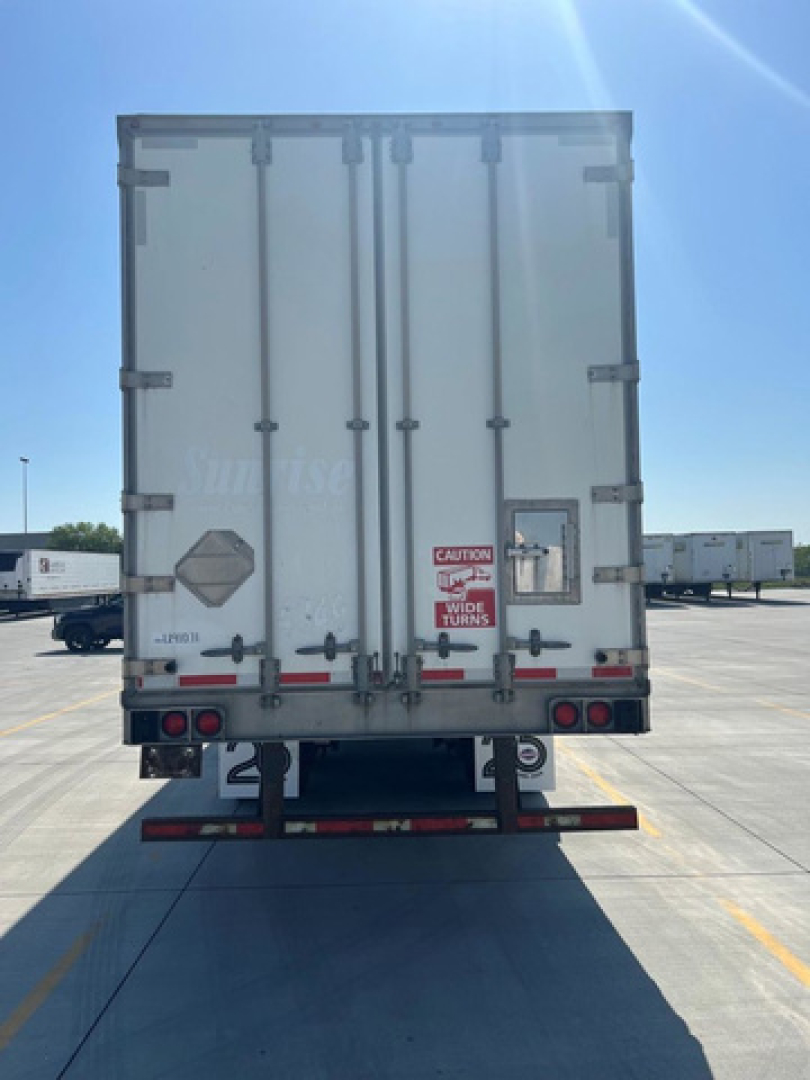 Rear view of a white 2014 utility van trailer with double doors, taillights, reflectors, and warning stickers; stock/ID and safety labels visible on doors.