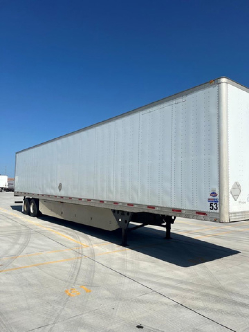 Trailer side view showing a white utility van trailer with tandem axles at rear and a small logo near the front corner.