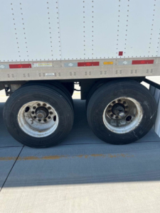 Dual rear tires on a utility trailer undercarriage with reflective tape and wheel rims visible.