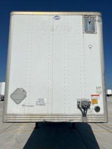 Rear view of a white utility van trailer showing VIN sticker, electrical connections, and small access doors.