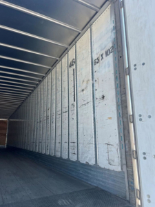 Interior of a 2014 utility van trailer showing metal walls with vertical riveted seams, numbered markings, and open side.