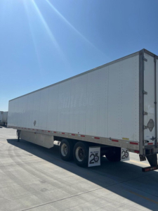 Trailer side view showing a white utility van trailer with dual rear axles and a 25 mph sign near the wheels.