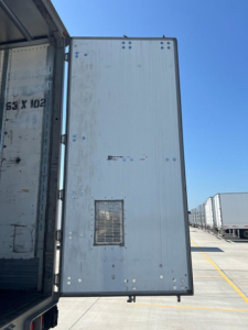 Trailer side door of a utility van showing a small rectangular vent and riveted metal exterior.
