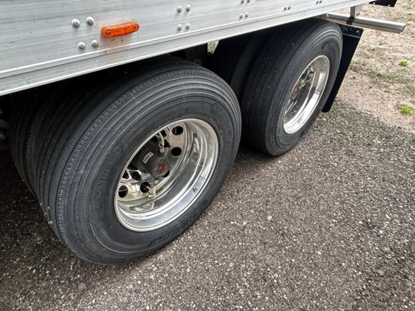 Rear side of a Utility 3000R trailer showing dual tandem wheels with silver rims and black tires, metal sidewall with rivets, small orange side marker light.