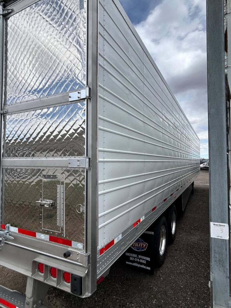 Utility 3000R trailer side view with aluminum ribbed siding and diamond plate rear access door; rear and side reflectors; tires visible under side view; small white label on post.