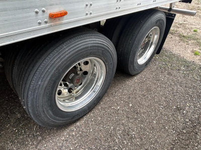 Rear side of a Utility 3000R trailer showing dual tandem wheels with silver rims and black tires, metal sidewall with rivets, small orange side marker light.