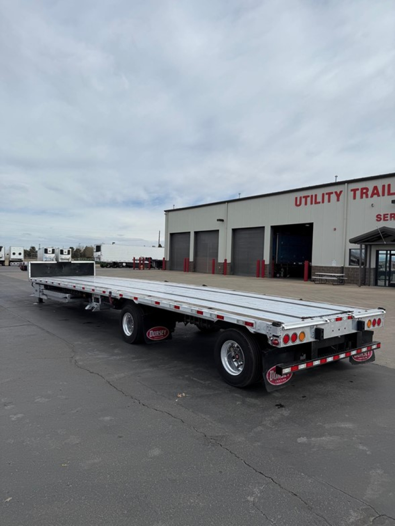 Flatbed trailer in a lot, side rails, dual rear axles, Dorsey combo drop deck trailer with aluminum deck and wheel wells visible.