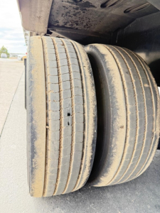 Trailer axle with dual tires showing tread and wheel ruts, undercarriage of a drop deck trailer.
