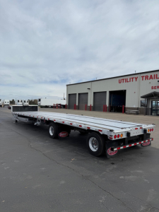 Used 2024 Dorsey combo drop deck trailer in a lot; aluminum drop deck with dual rear axles and company building in background.