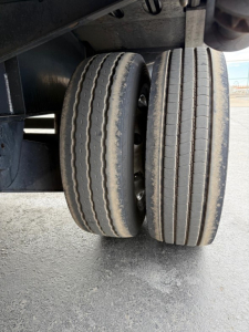 Dual rear trailer wheels on a drop deck trailer showing two axial tires with tread grooves and underside structure.