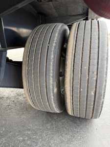 Dual trailer wheels showing worn tire tread on left and right with visible road grime; tandem axle setup under trailer frame.
