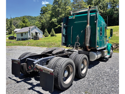 Tri-axle Freightliner Coronado tractor rear view showing green cab, fifth wheel, and dual rear axles with dual tires.