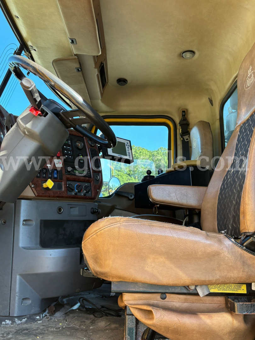 Cab interior of a 2009 Mack GU713 dump truck showing steering wheel, dashboard, and tan worn seats with controls and gauges visible.