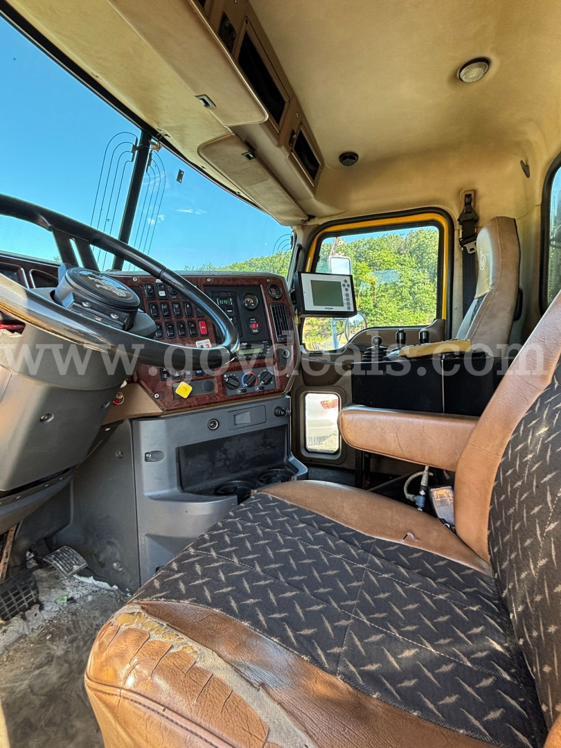 Truck cab interior showing steering wheel, dashboard, and driver seat of a Mack GU713, with a mounted tablet/GPS on the dash. Visible text includes faint dealership watermark 'www.govdeals.com' across the windshield.