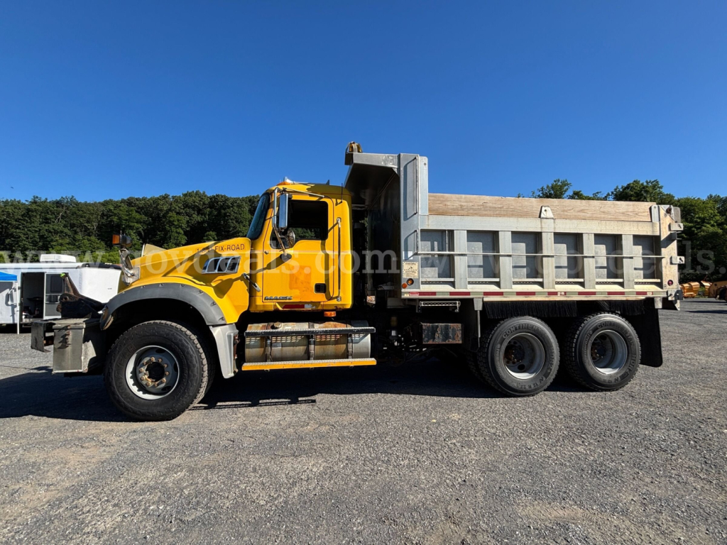 Dump truck body with a yellow Mack GU713 cab and gray dump bed, side view showcasing dual rear axles and heavy-duty tires.