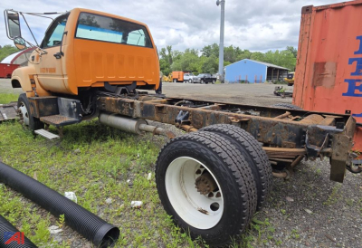 GMC cab and chassis truck frame with orange cab, large rear wheel, and rusted chassis showing exposed frame rails.