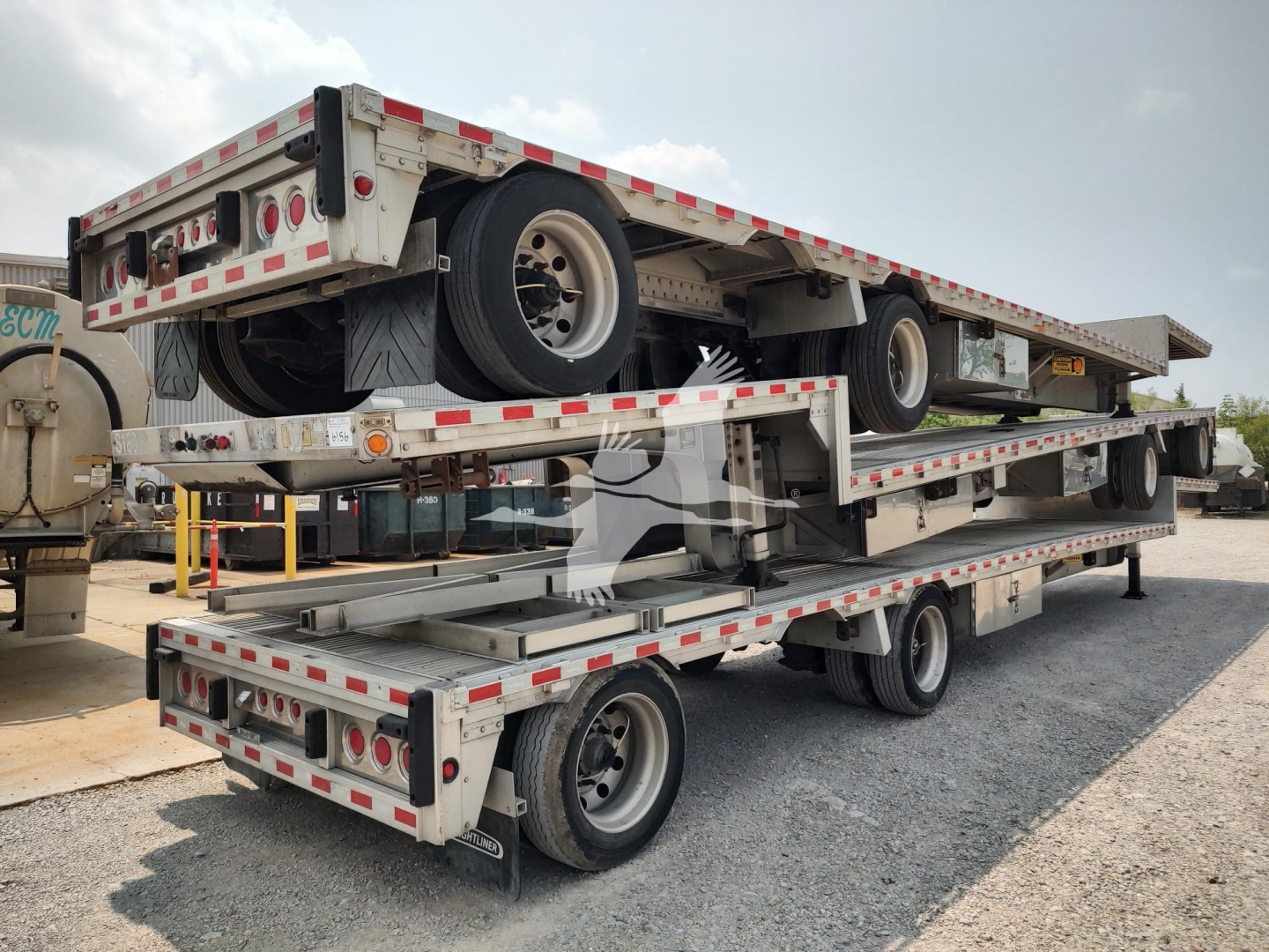 Trailer deck showing stacked flatbed trailers on a multi-axle transporter, 2018 Reitnouer Dropmiser, with visible rear lights and reflective safety tape.