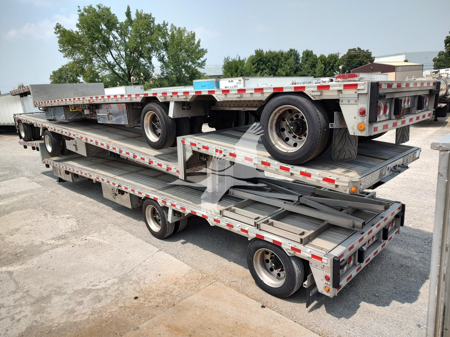 Trailer stack showing multiple flatbed decks and spare tire on a drop deck trailer.