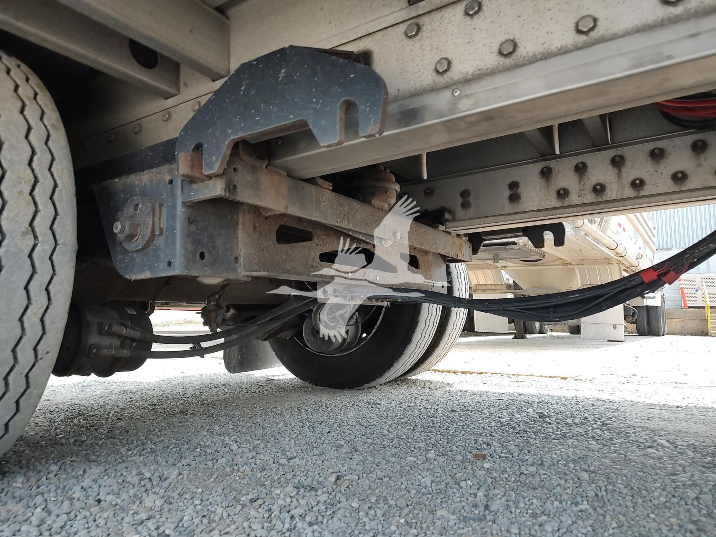 Trailer undercarriage showing suspension leaf springs and frame with hoses and wiring visible near wheel