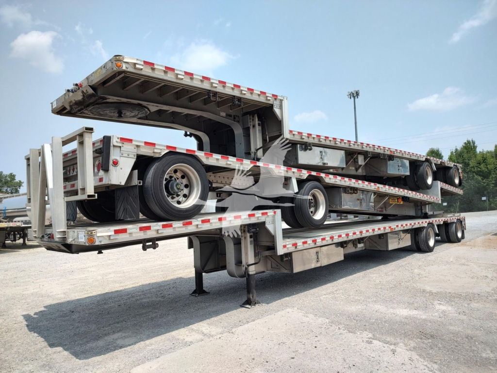 Trailer showing a stacked drop deck trailer with multiple axles and access ramp in a yard.