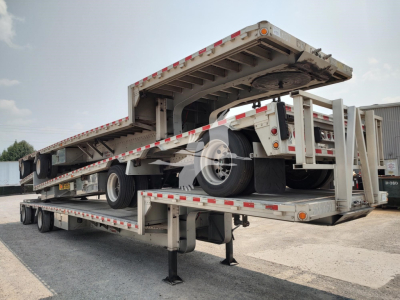 Drop deck trailer in raised position showing tandem axle and landing gear with reflective tape and wheel rims.