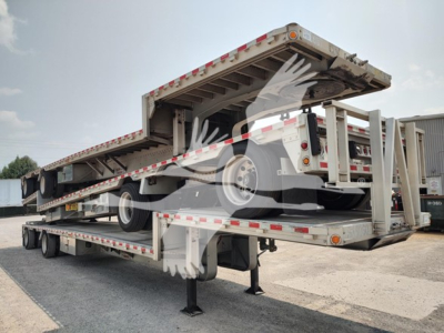 Drop deck trailer in transport position with hydraulic drop mechanism visible and reflective tape along sides.