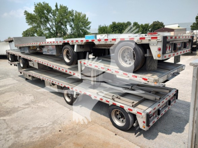 Dropdeck trailer stacks showing multiple levels with metal decks and a spare tire; side rails with reflective tape; metal frames and tires visible.