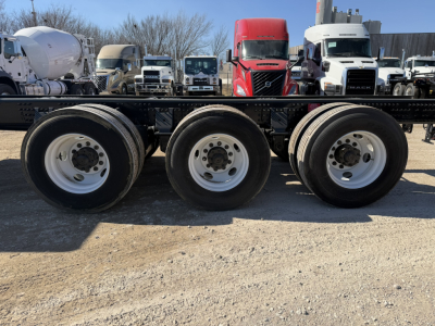Volvo VHD86B300 cab and chassis wheelset view showing triple rear axle wheels and surrounding trucks in a lot.