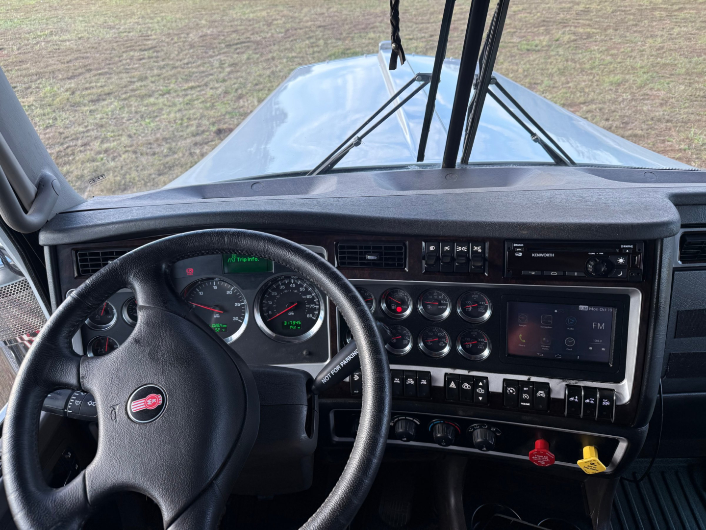 Kenworth W900L cab interior showing steering wheel, instrument cluster, and dashboard controls with gauges and digital display