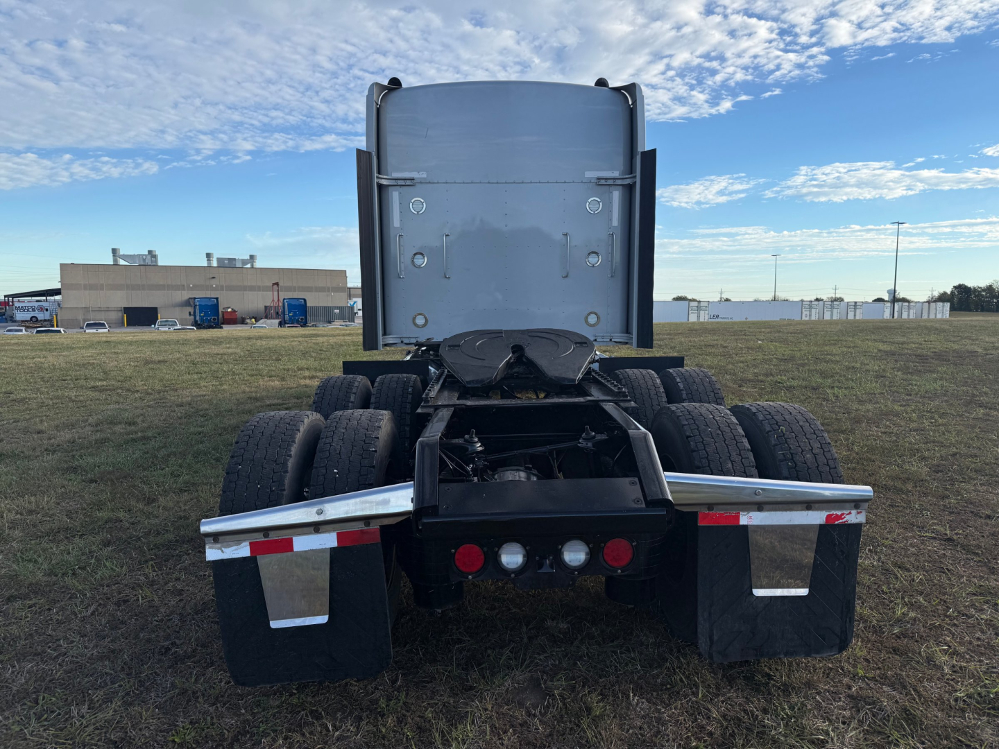 Kenworth W900L rear view showing fifth wheel, dual rear axles, and mud flaps; back of cab with vertical exhaust stacks and taillights visible.