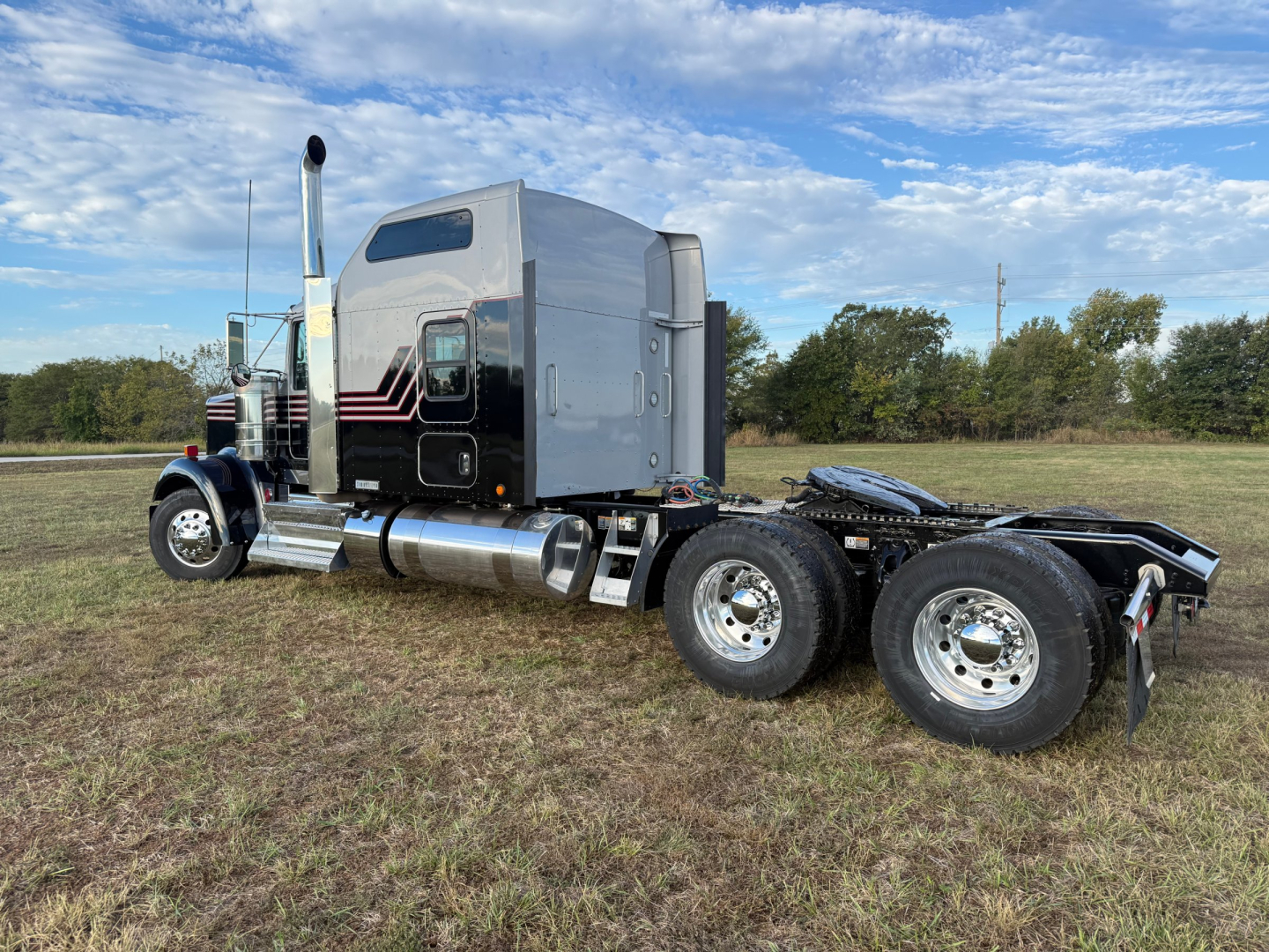 Kenworth W900L tractor cab in side profile showing aluminum fuel tanks and dual rear axles with chrome wheels.
